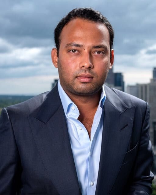 Portrait of Leander D’Silva in a dark suit, with a city skyline behind him.